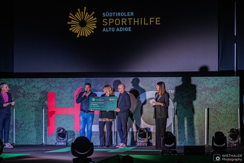 Sporthilfe Präsident Dr. Giovanni Podini (2. v. l.) durfte im Rahmen der HERO Fashion Night einen Scheck von 5.000,00 Euro entgegennehmen und bedankte sich von ganzem Herzen bei OK-Chef Gerhard Vanzi (4. v. l.) für die erneute großzügige Unterstützung (Photocredit BMW HERO Südtirol Dolomites 2023_@wisthaler).