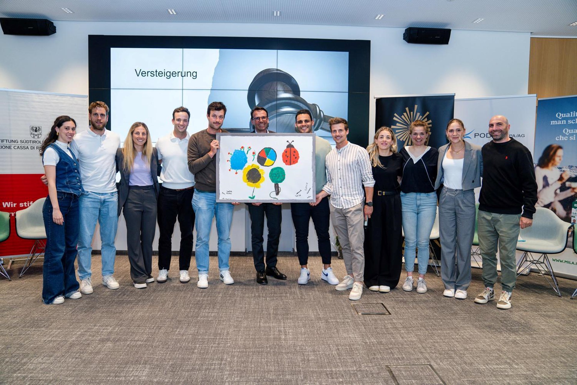 Die Heimbewohner des KIMM haben die Olympischen Ringe neu interpretiert; das Bild wurde im Mai beim Abschluss des Great Season Ausbildungsprogramm versteigert. Im Bild die Teilnehmer:innen und Christoph Kasslatter von Markas.